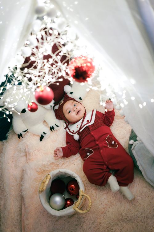 Free Cute baby in red Christmas outfit surrounded by holiday decorations and lights. Stock Photo