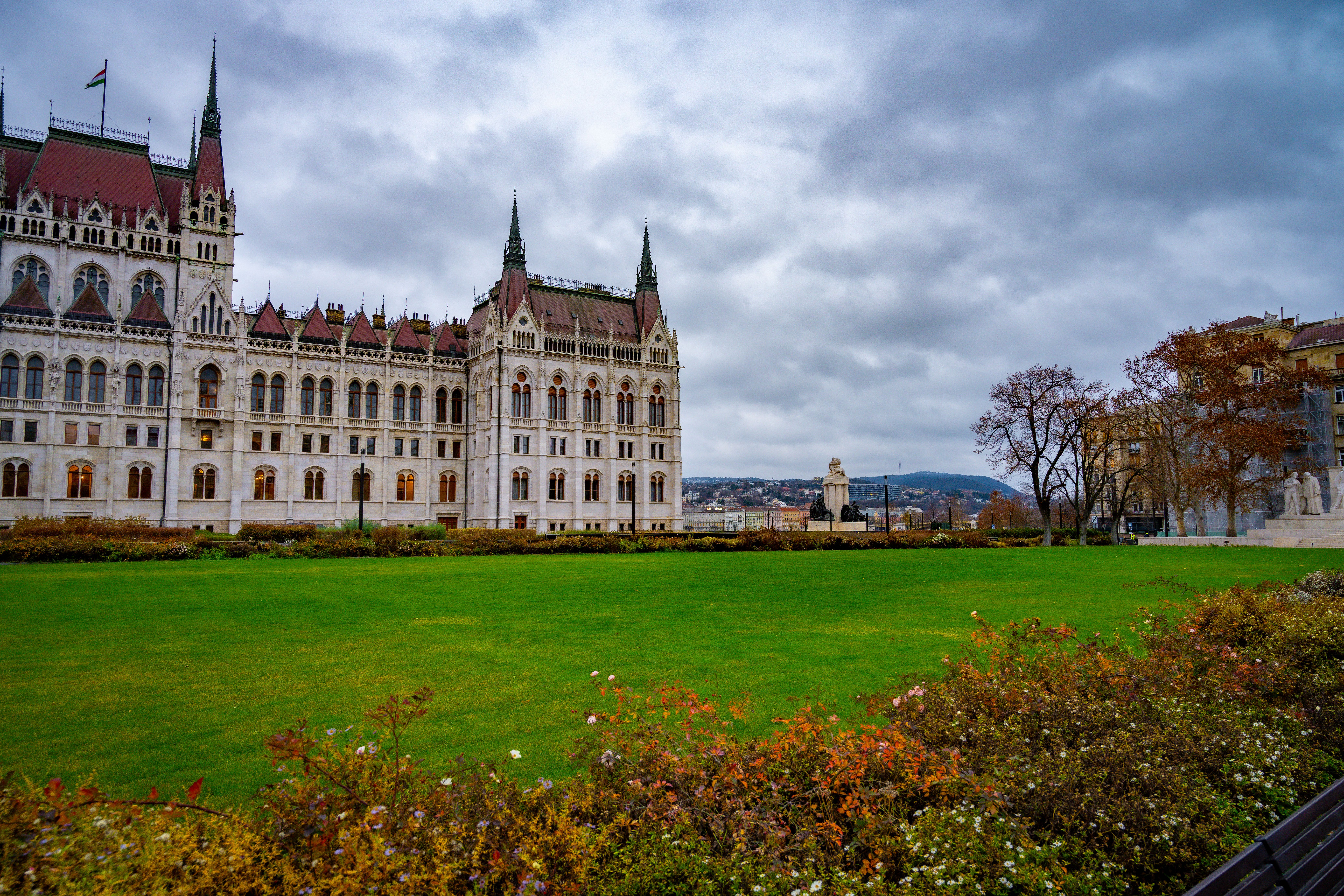 Scenic view of Budapest's Hungarian Parliament with lush green gardens and cloudy sky.