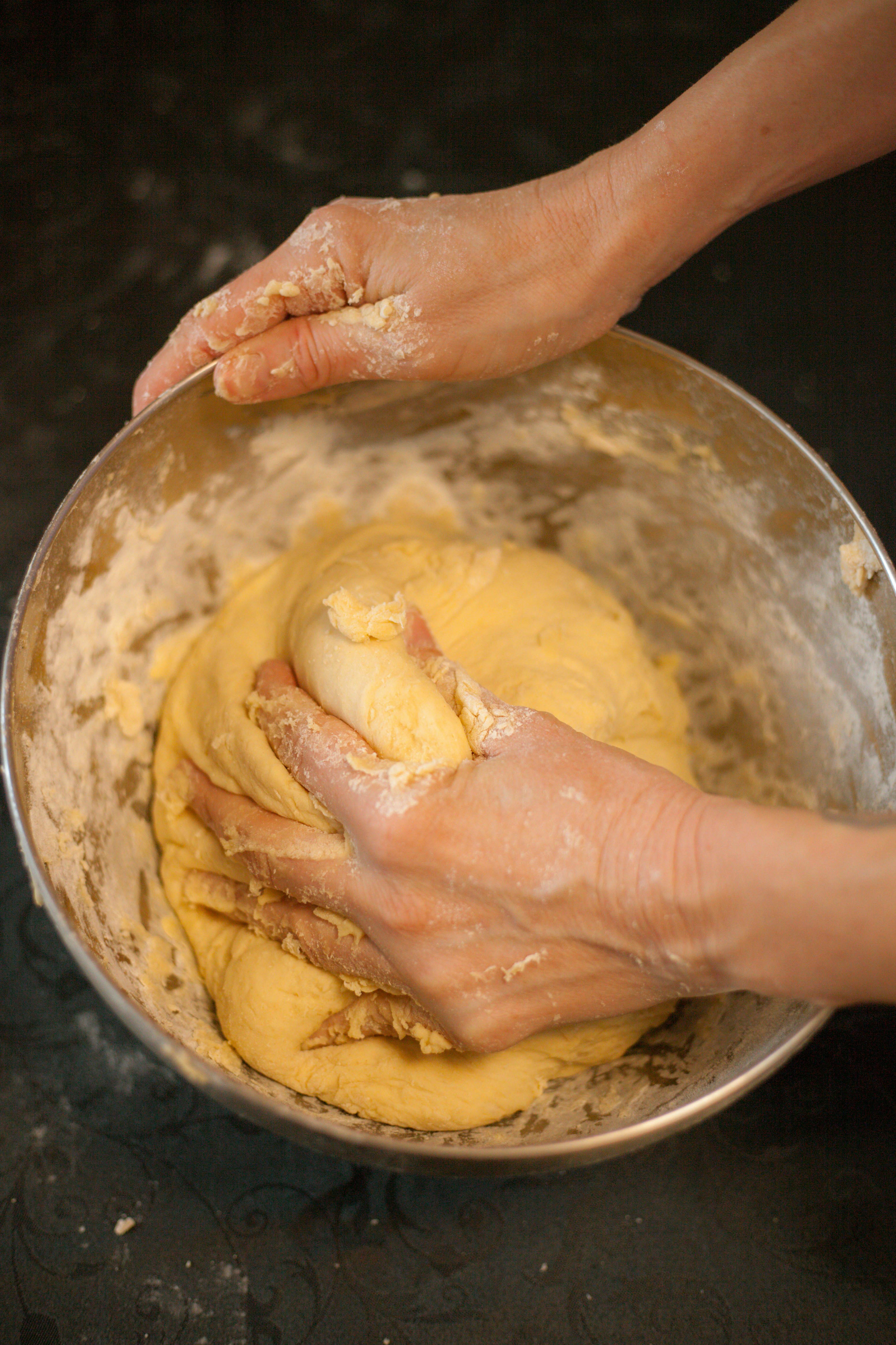 A person's hands kneading dough in a metal bowl, preparing it for baking.