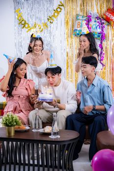 A group of adults celebrating a birthday with cake and party hats in a festive setting.