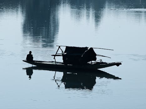 A lone person on a wooden boat on a calm lake at dawn with muted reflections.