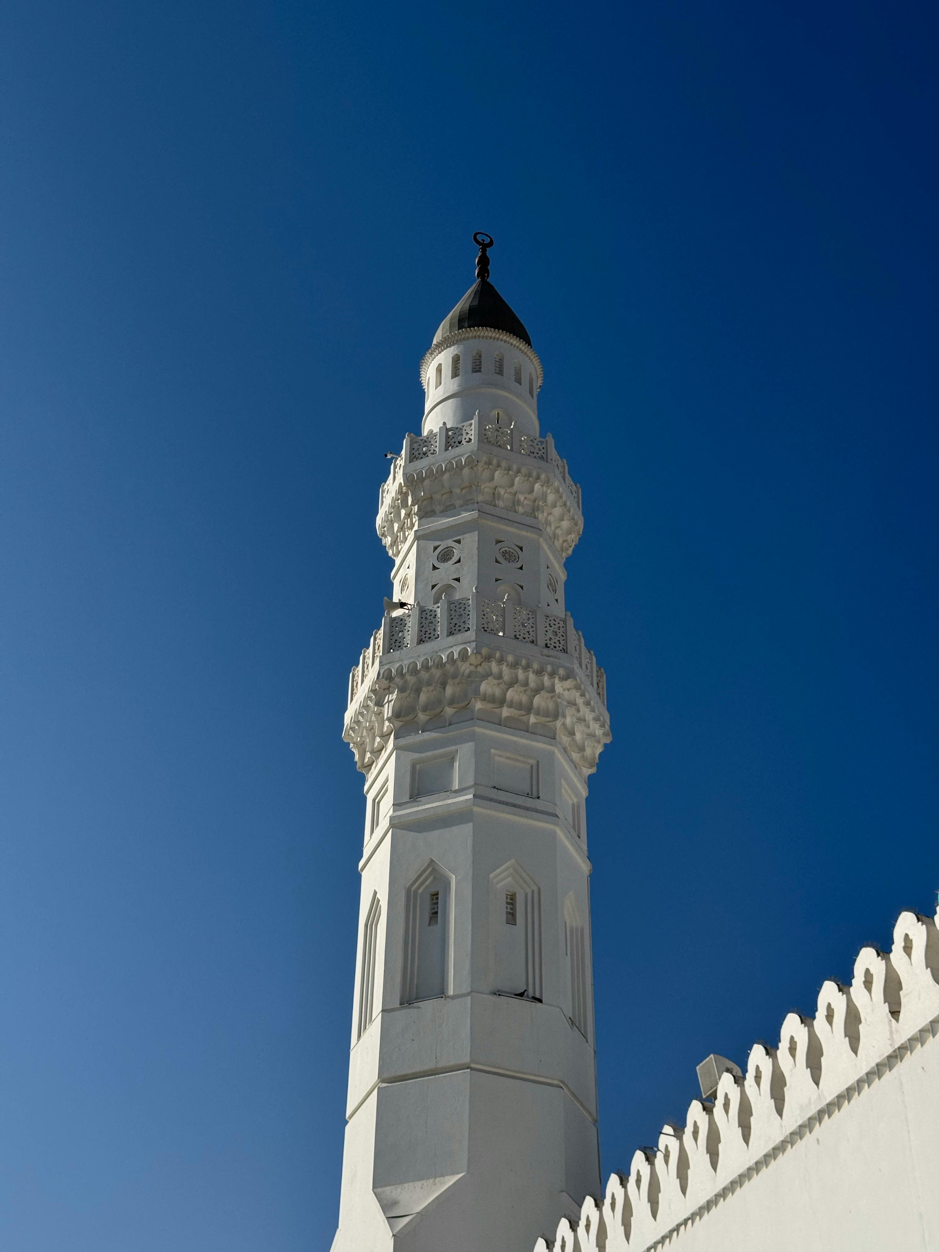 Stunning view of a white Islamic minaret under a vivid blue sky, showcasing architectural beauty.