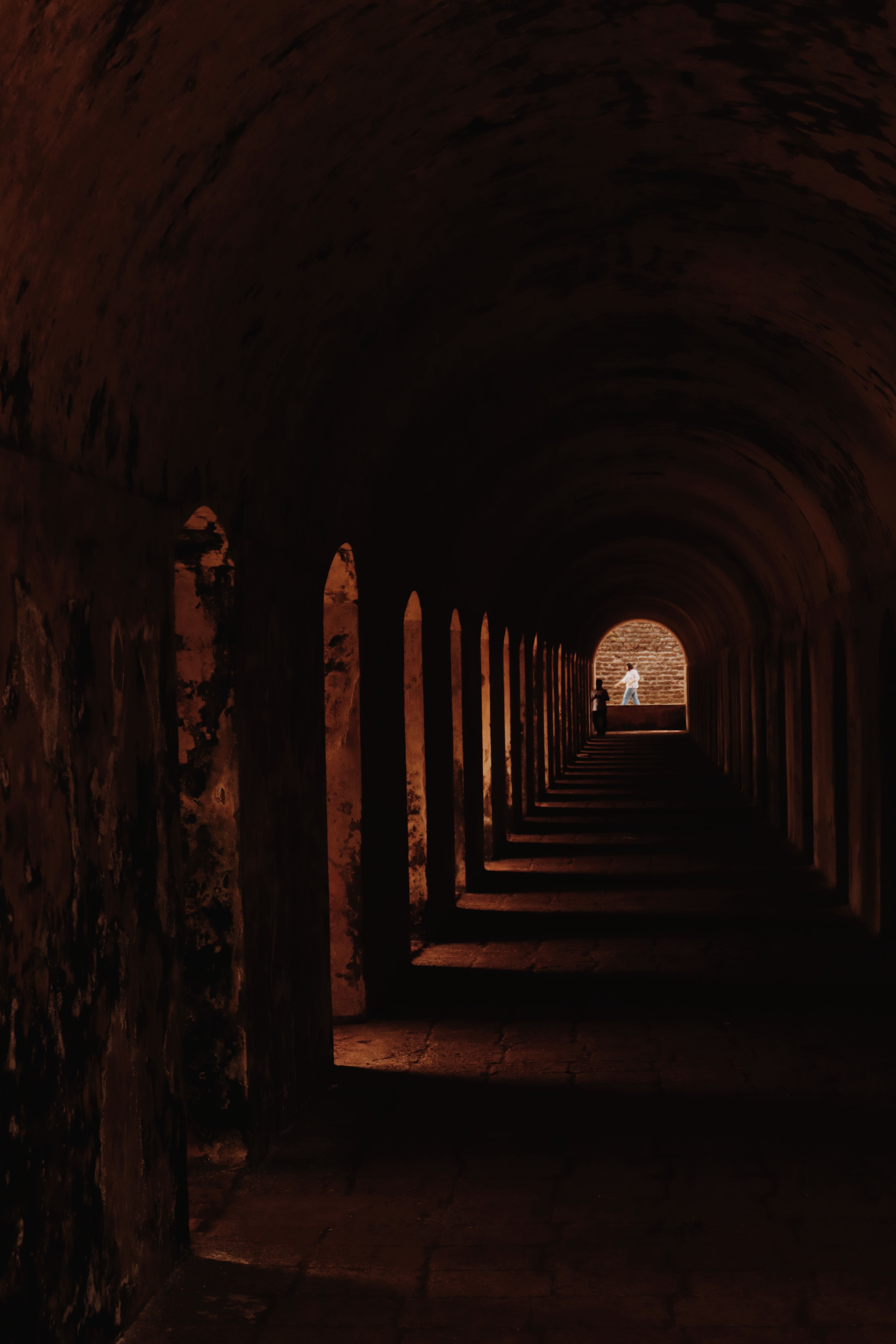 Gratuit Un long tunnel sombre à l'éclairage tamisé, avec une silhouette illuminée au bout. Spectaculaire et mystérieux. Photos