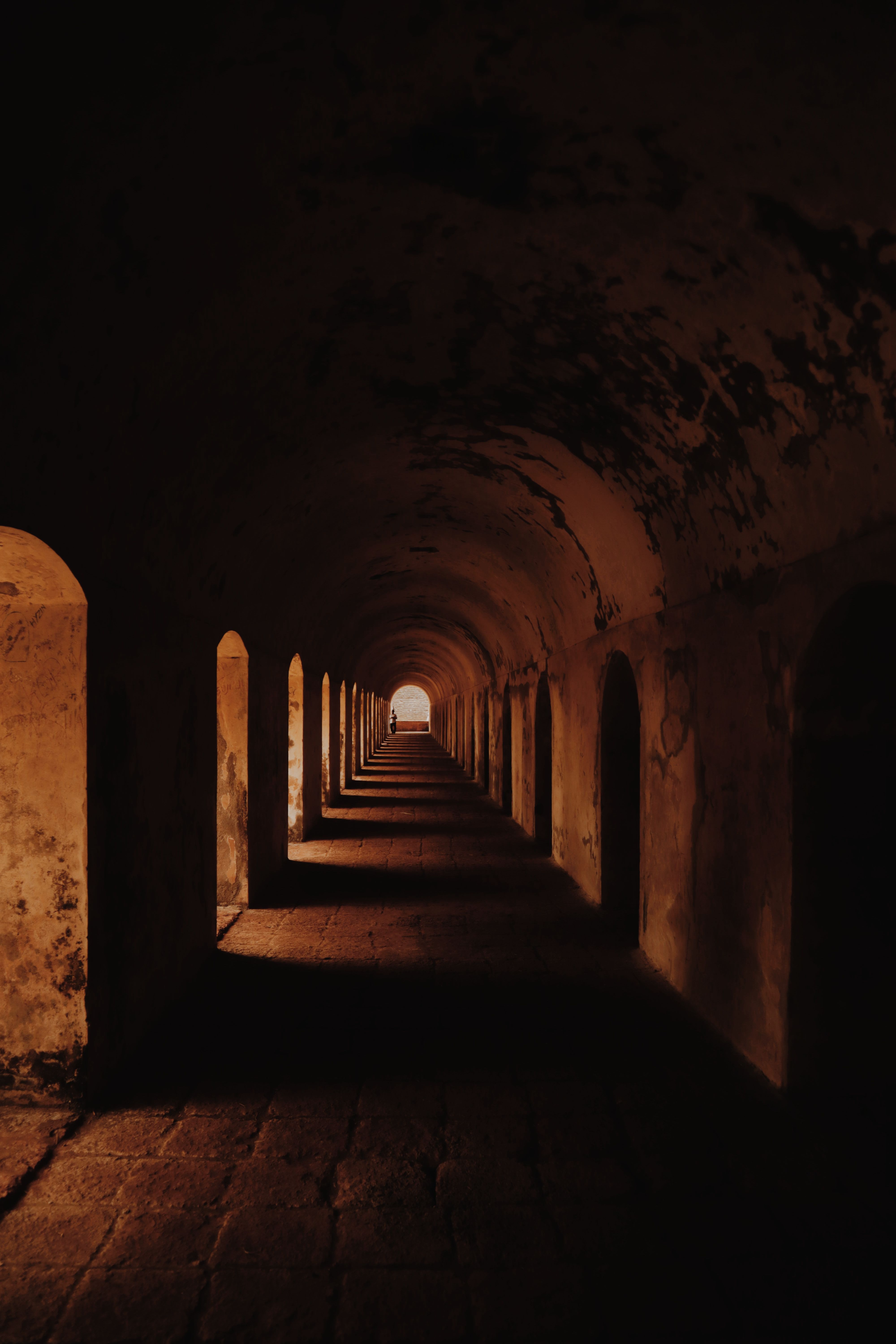 Gratuit Explorez un tunnel sombre et mystérieux, orné d'arches menant à une lumière lointaine. Photos