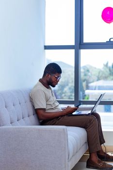 Businessman multitasking on a couch with a laptop and phone indoors.