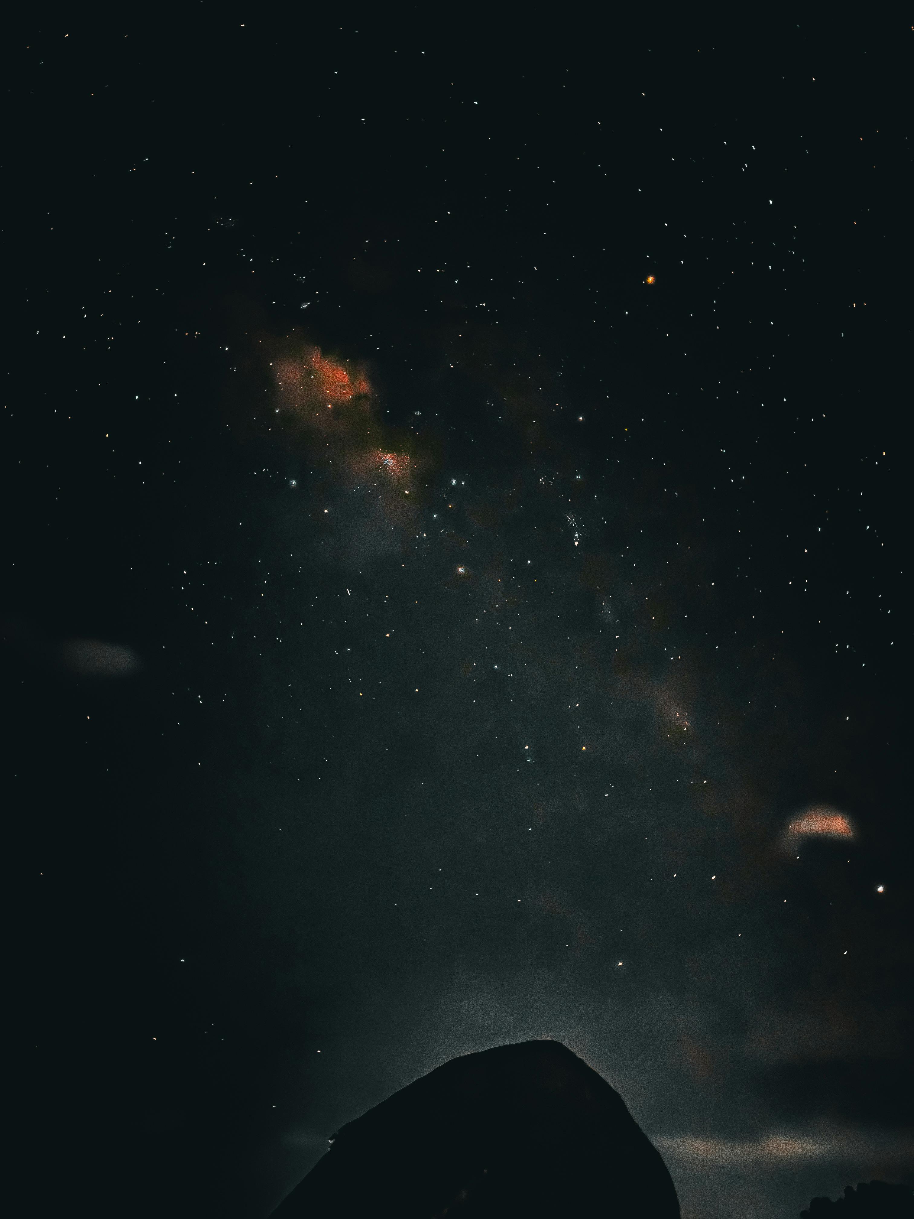 grátis Uma vista deslumbrante do céu estrelado à noite, com a Via Láctea acima de uma colina que recorta sua silhueta. Foto profissional