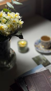 A serene tabletop with daffodils, coffee, books, and a candle.