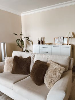 A stylish and cozy living room featuring a white sofa with fluffy cushions and modern decor.