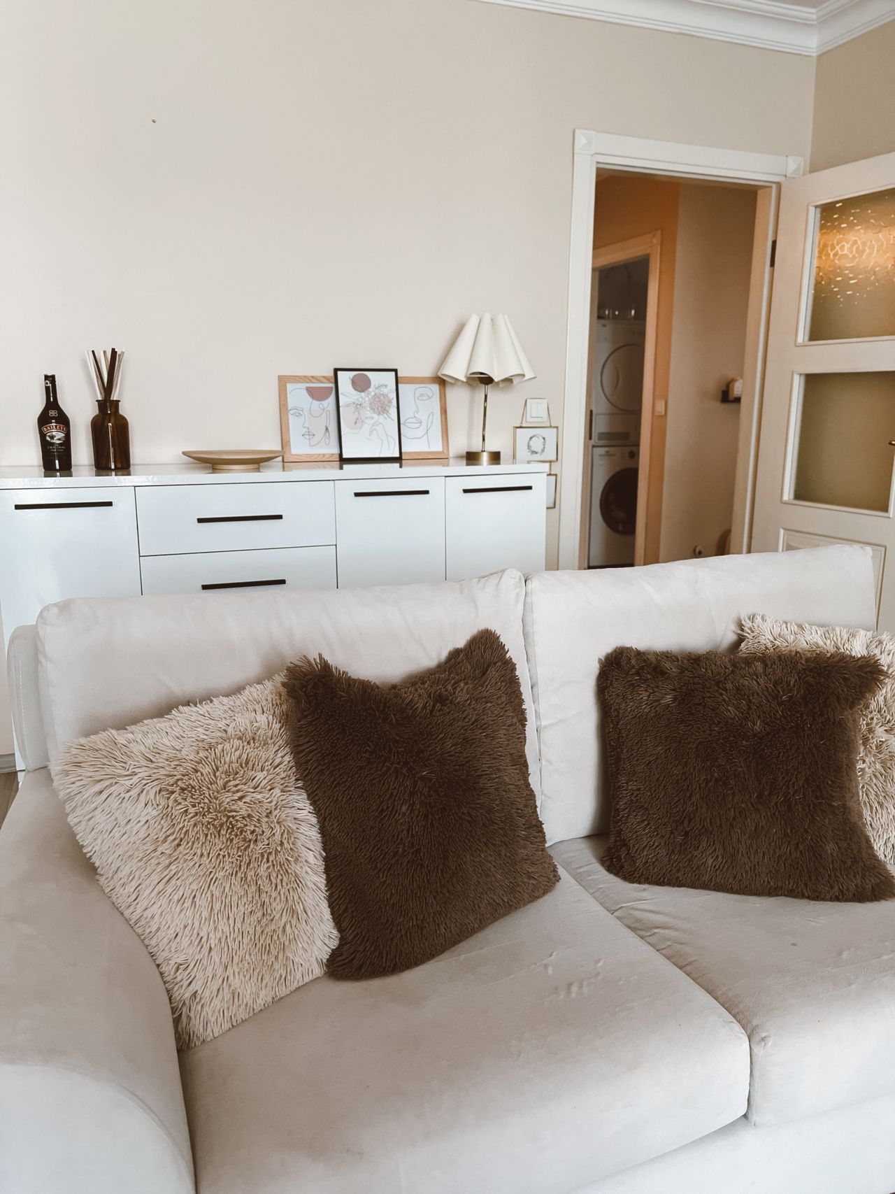 Cream sofa with warm neutral cushions, sideboard and table lamp