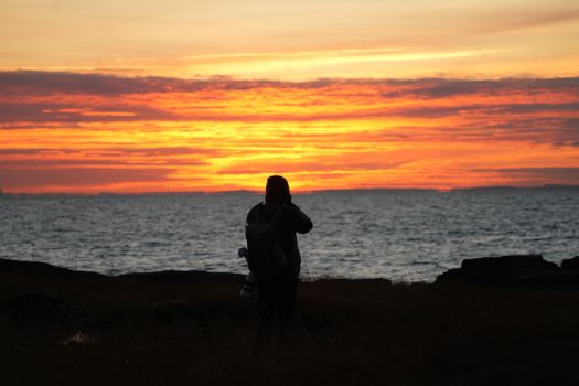 Silhouette of a person with a camera capturing a stunning sunset over the sea.