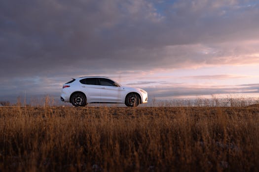 A white SUV parked on a rural road under a colorful sunrise sky.