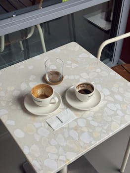 Overhead view of two empty coffee cups and a glass on a modern cafe table.