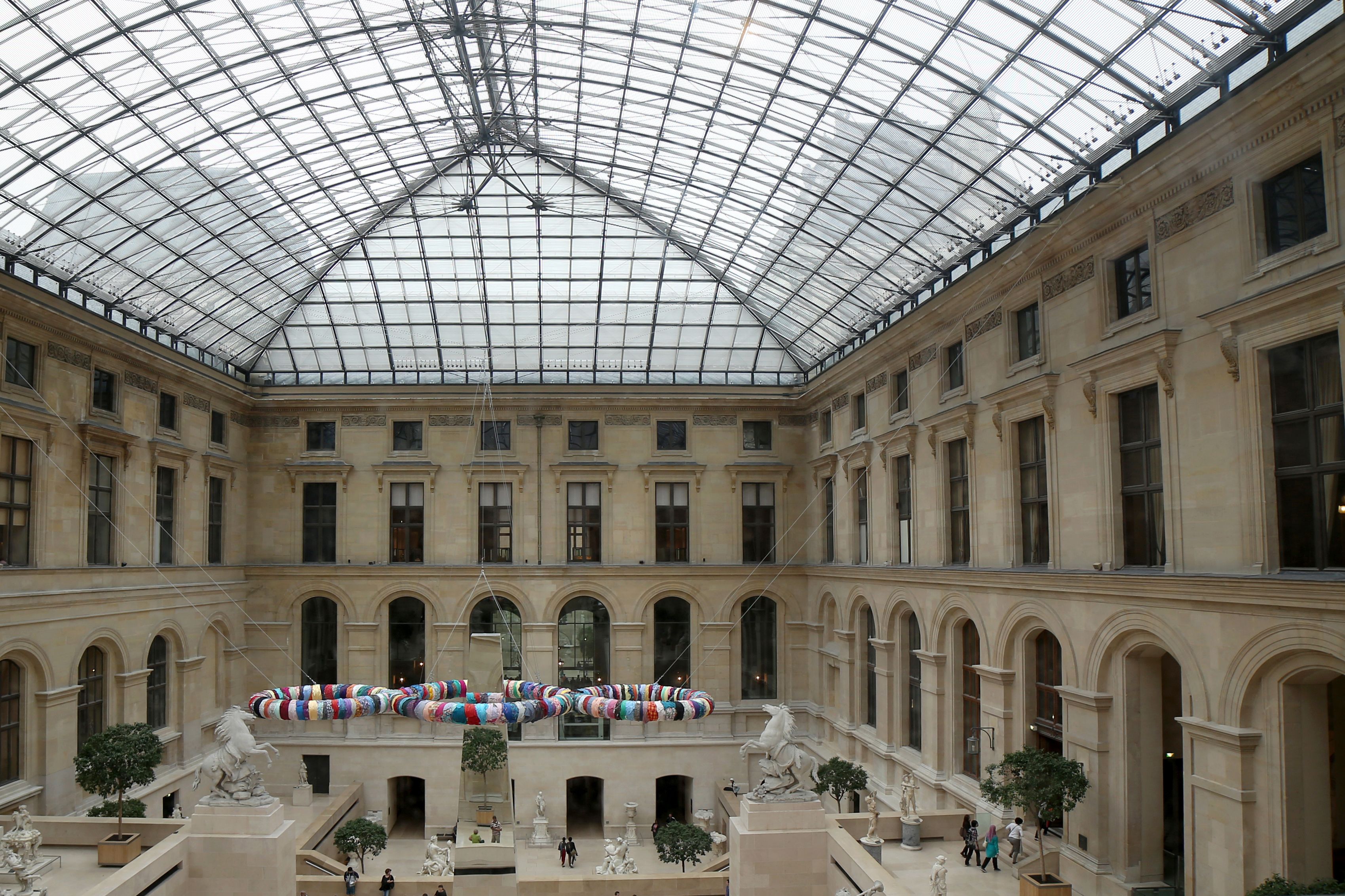 The Louvre Museum's glass-roofed courtyard with classic stone architecture and arched windows.