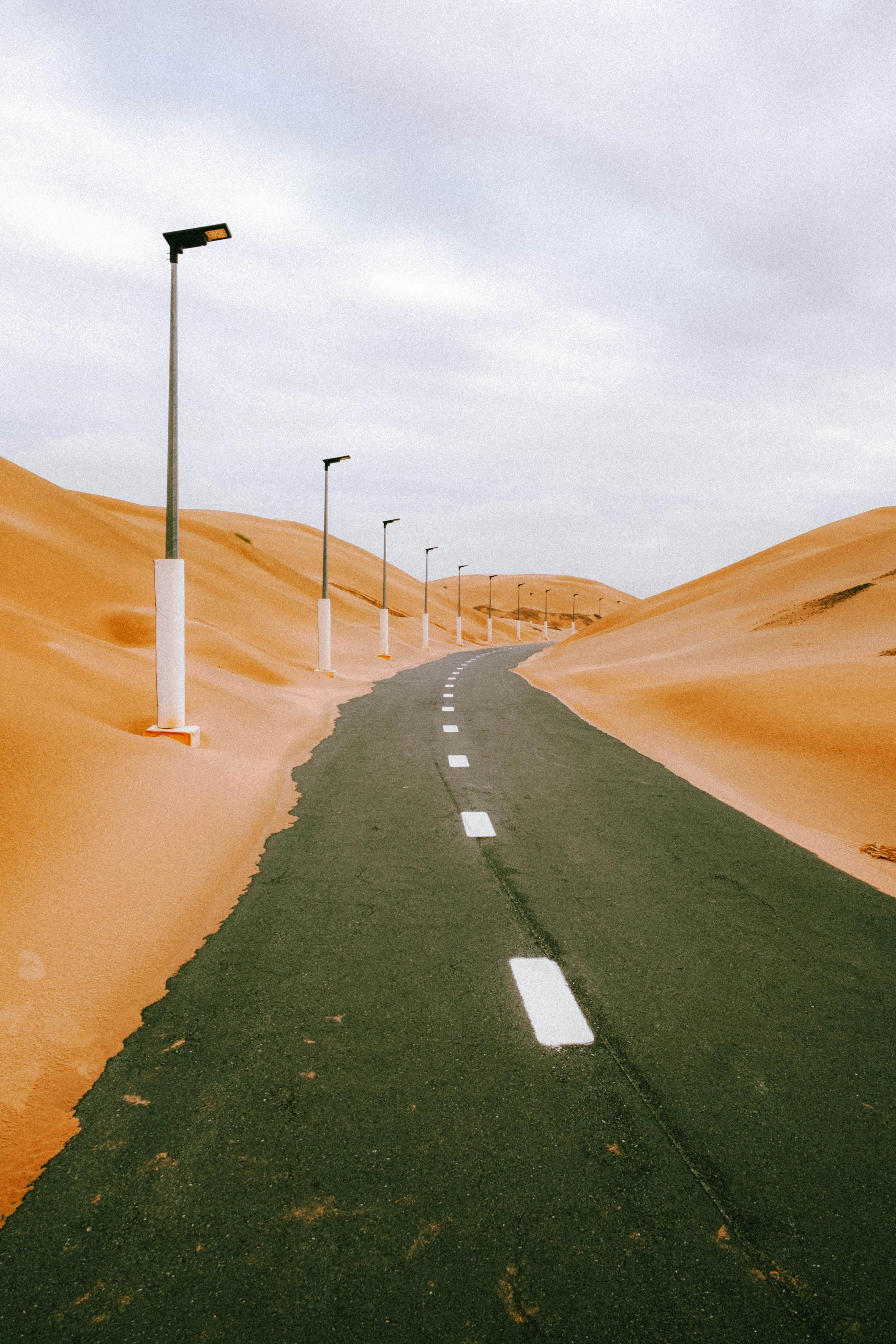 Scenic road flanked by desert dunes under cloudy skies in Abu Dhabi, UAE.