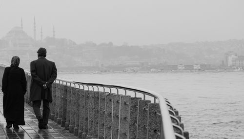Free Black and white photo of a couple walking along Istanbul's waterfront with a mosque in the background. Stock Photo