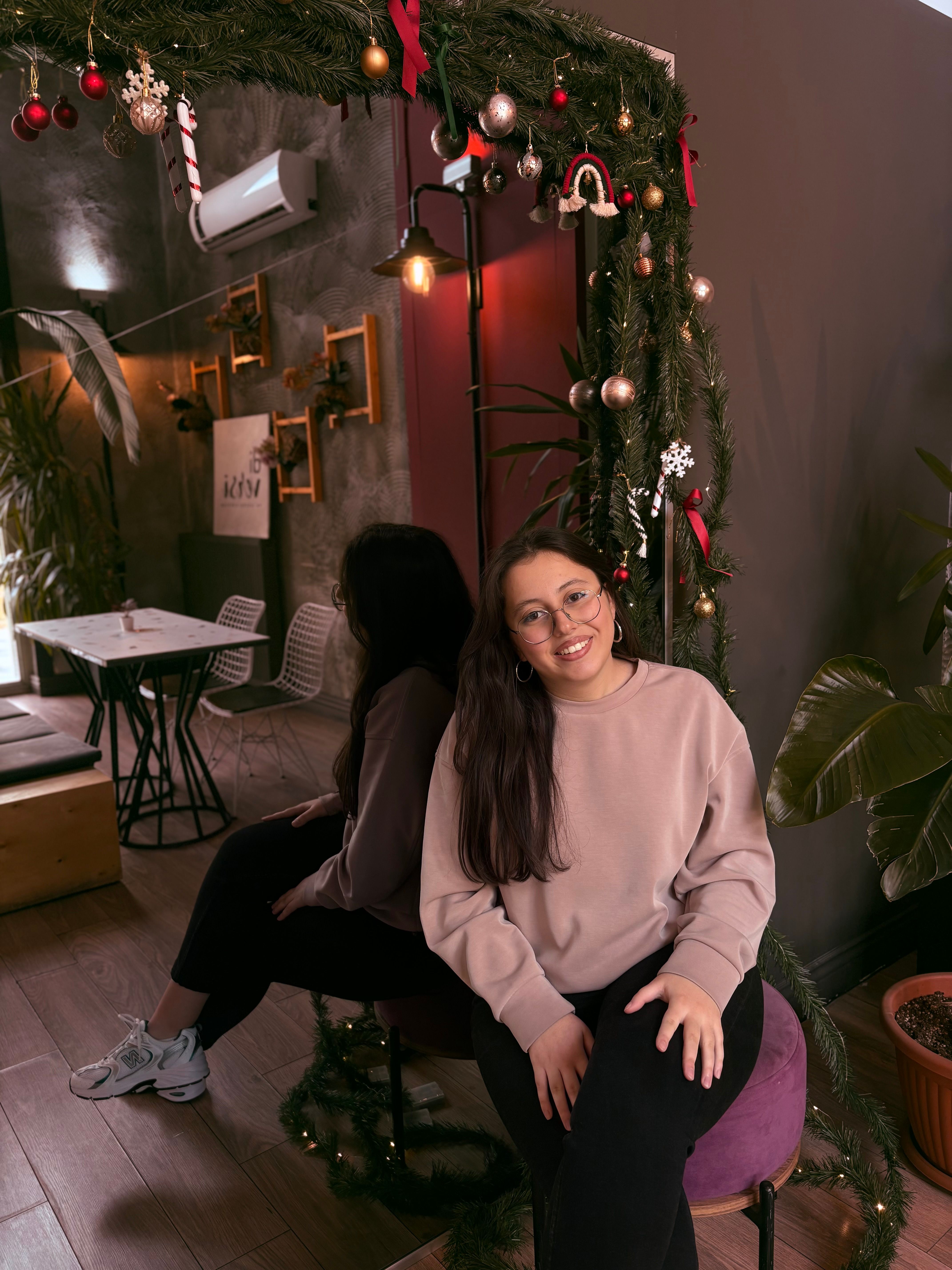 Woman sitting in a cozy indoor setting with holiday decorations, smiling warmly.