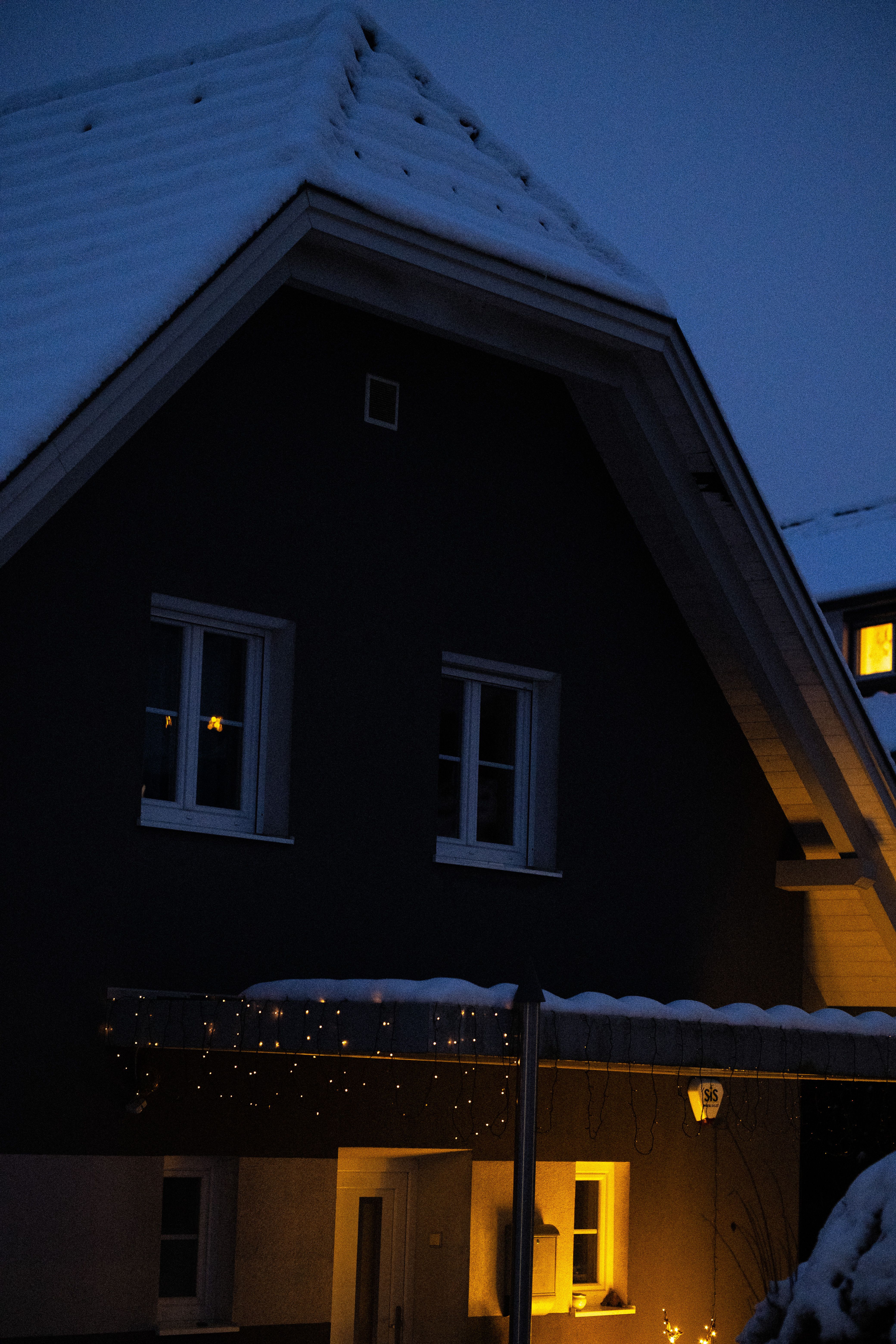 A cozy snow-covered house with warm glowing lights in the night.