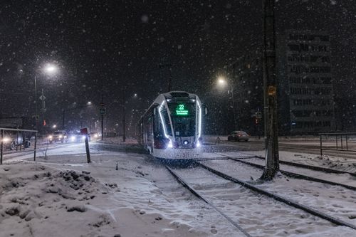 Free A tram travels through a snowy city street at night, illuminated by streetlights. Stock Photo