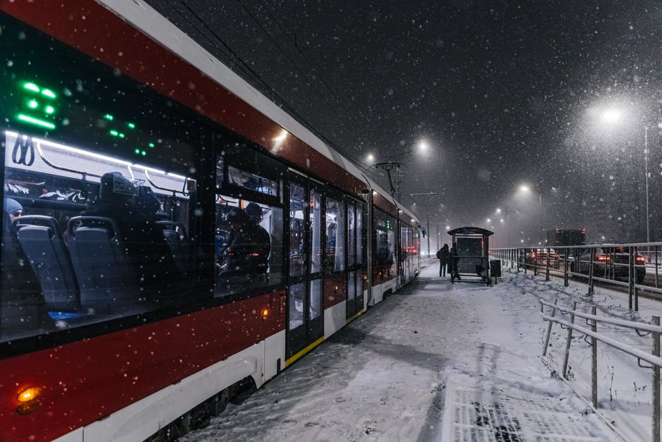A red tram at a snowy stop on a winter's night, capturing urban life.