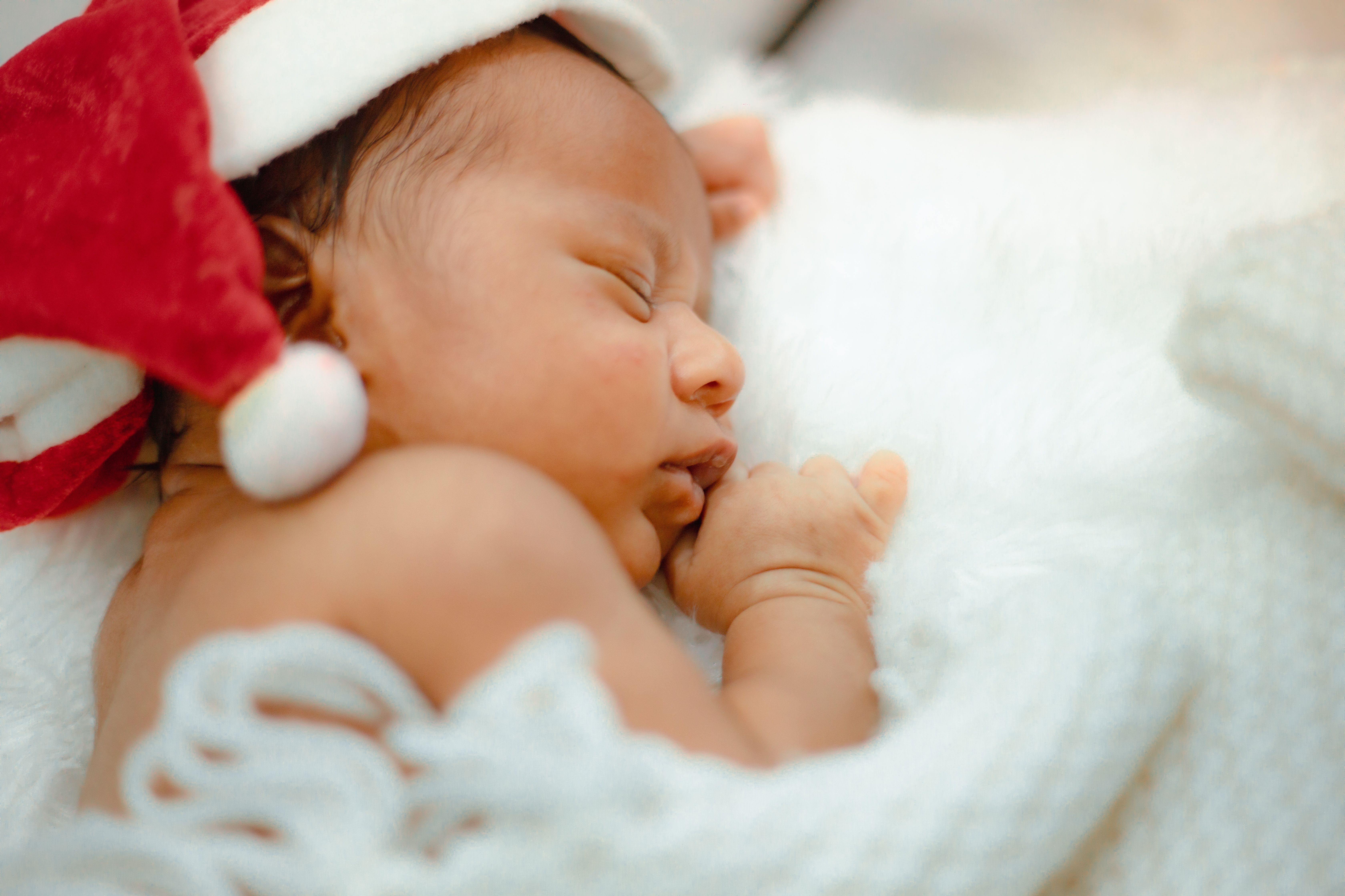 Cute newborn baby sleeping peacefully wearing a Santa hat, representing the warmth of the holiday season.