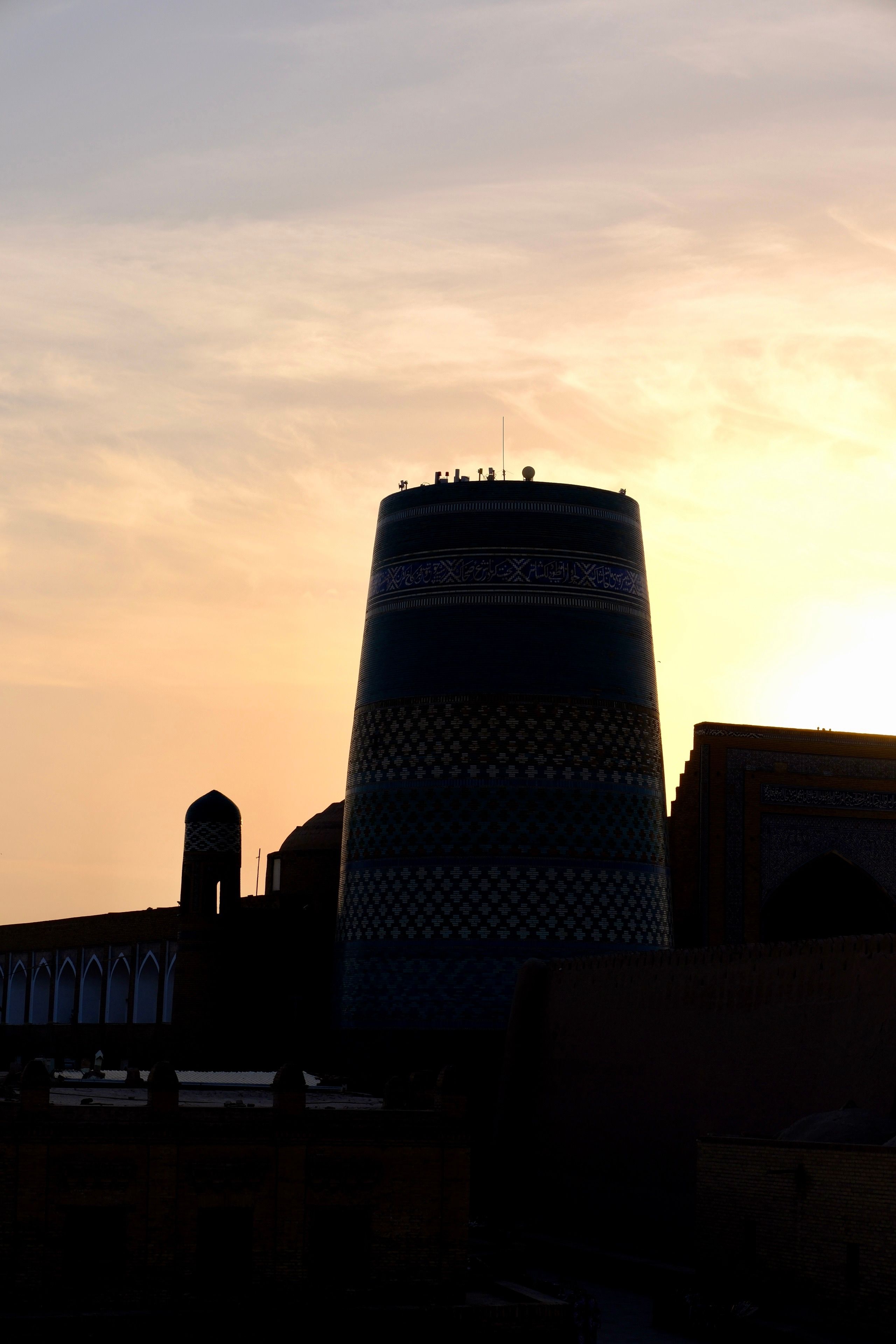 The Kalta Minor Minaret stands silhouetted against a vibrant sunset in Khiva, highlighting its colorful, intricate tiles.