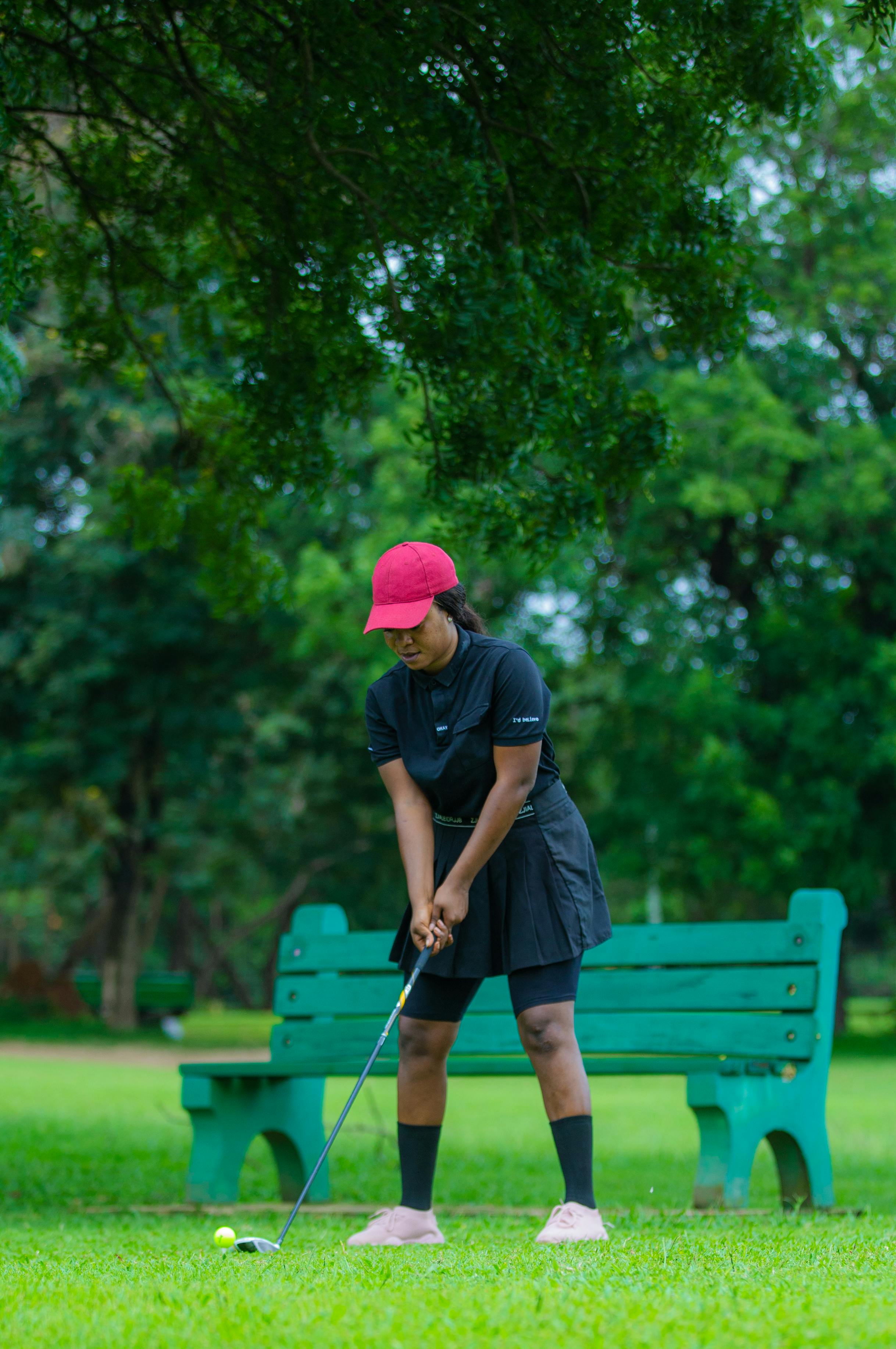 A woman golfer in a park setting, ready to hit the ball, showing focus and determination.