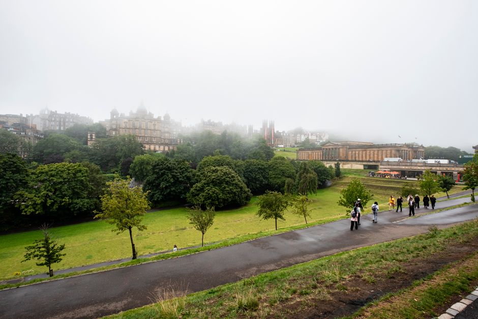 Misty day at Calton Hill, Edinburgh with lush trees, paths, and distant classical architecture.