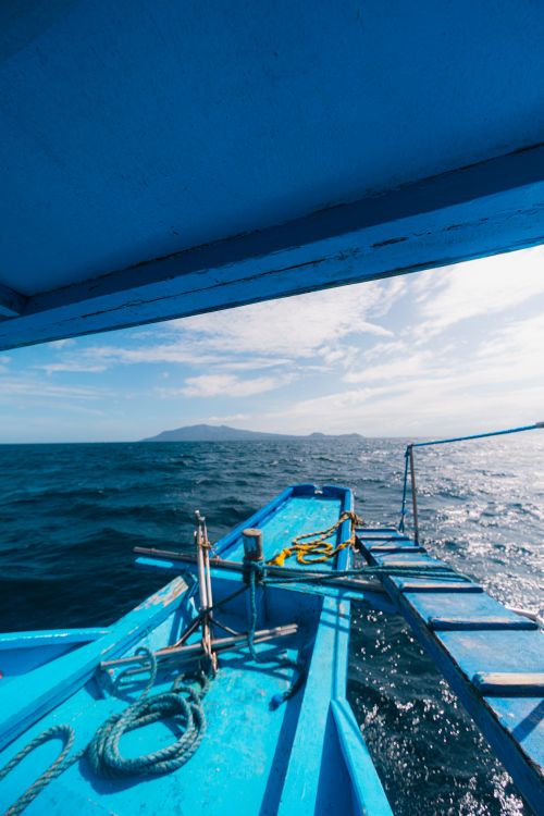 Free A vibrant blue boat sailing on a sunny day with clear skies and mountain views in the distance. Stock Photo