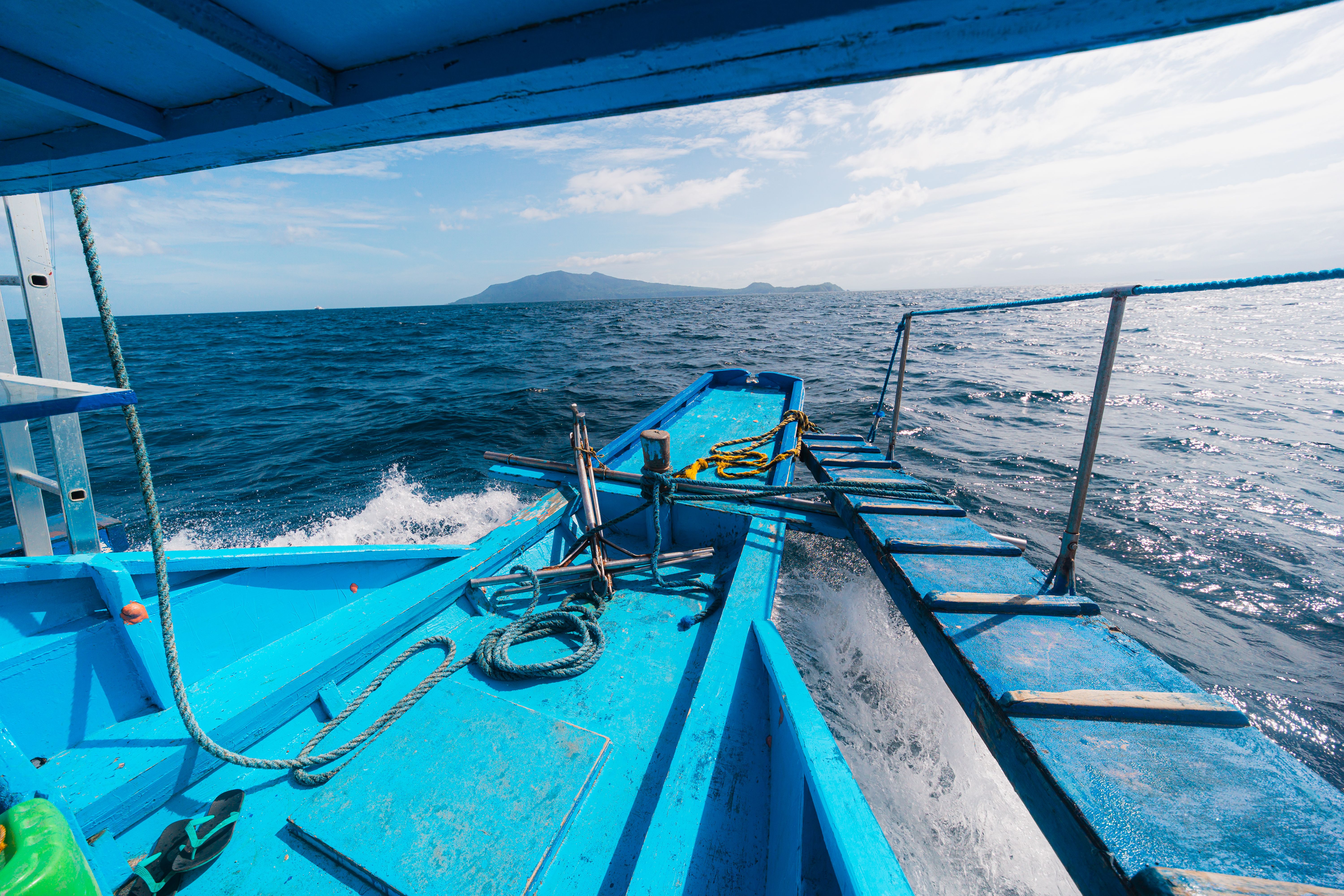 Blue Boat Navigating Ocean Waters with Distant Island · Free Stock Photo
