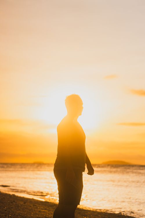 Free Silhouette of a person standing by the sea during a vivid sunset, creating a peaceful beach atmosphere. Stock Photo