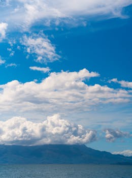 Beautiful ocean view with mountains and fluffy clouds against a vibrant blue sky.