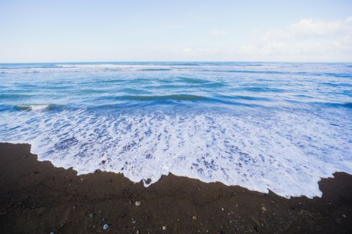 Free Serene coastal scene of ocean waves gently hitting a sandy beach under a clear blue sky. Stock Photo