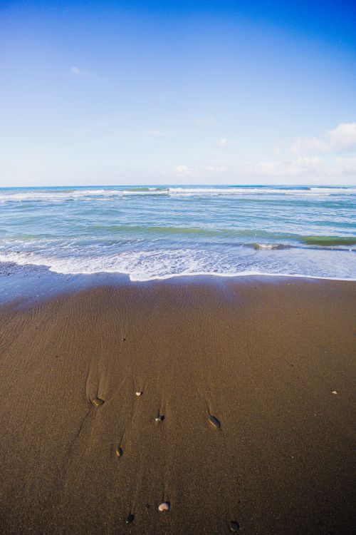 Free A serene view of ocean waves gently touching a sandy beach under a clear blue sky. Stock Photo