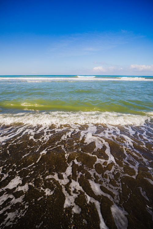 Free Tranquil ocean waves at the shore under a vibrant blue sky, perfect for relaxation themes. Stock Photo