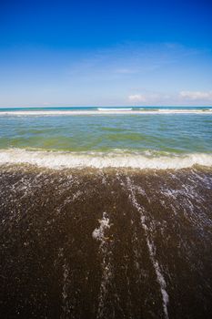 Capture of ocean waves lapping a sandy beach under a clear blue sky.
