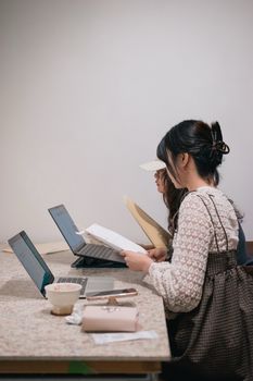 Two young women intensely studying at laptops in a cozy indoor setting.