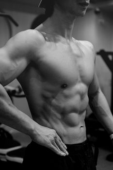 Black and white photo of a muscular male torso in a gym environment, highlighting abs and fitness.