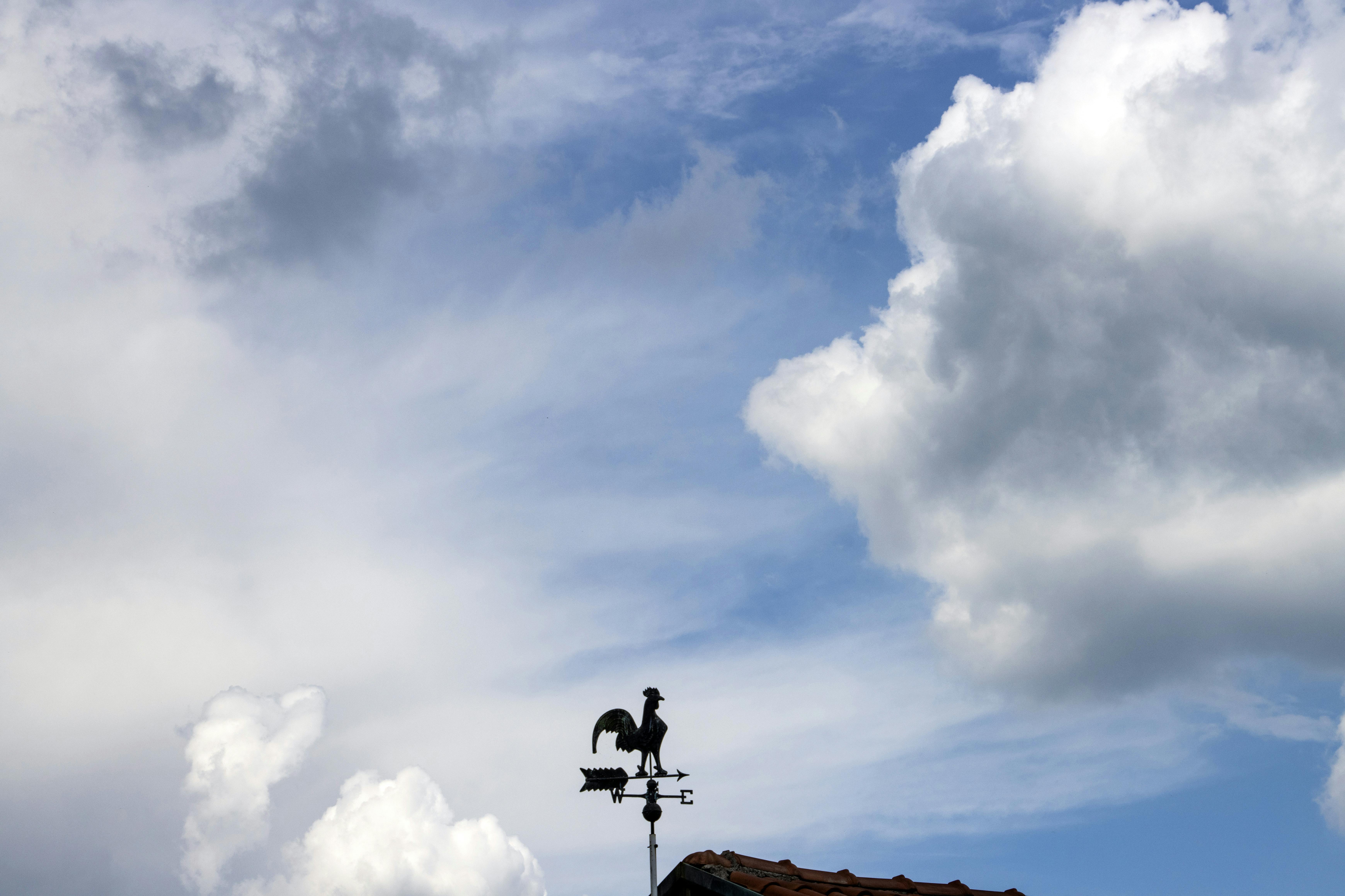 Kostenlos Eine Wetterfahne, die sich vor einem hellen, wolkenverhangenen Himmel abzeichnet. Stock-Foto