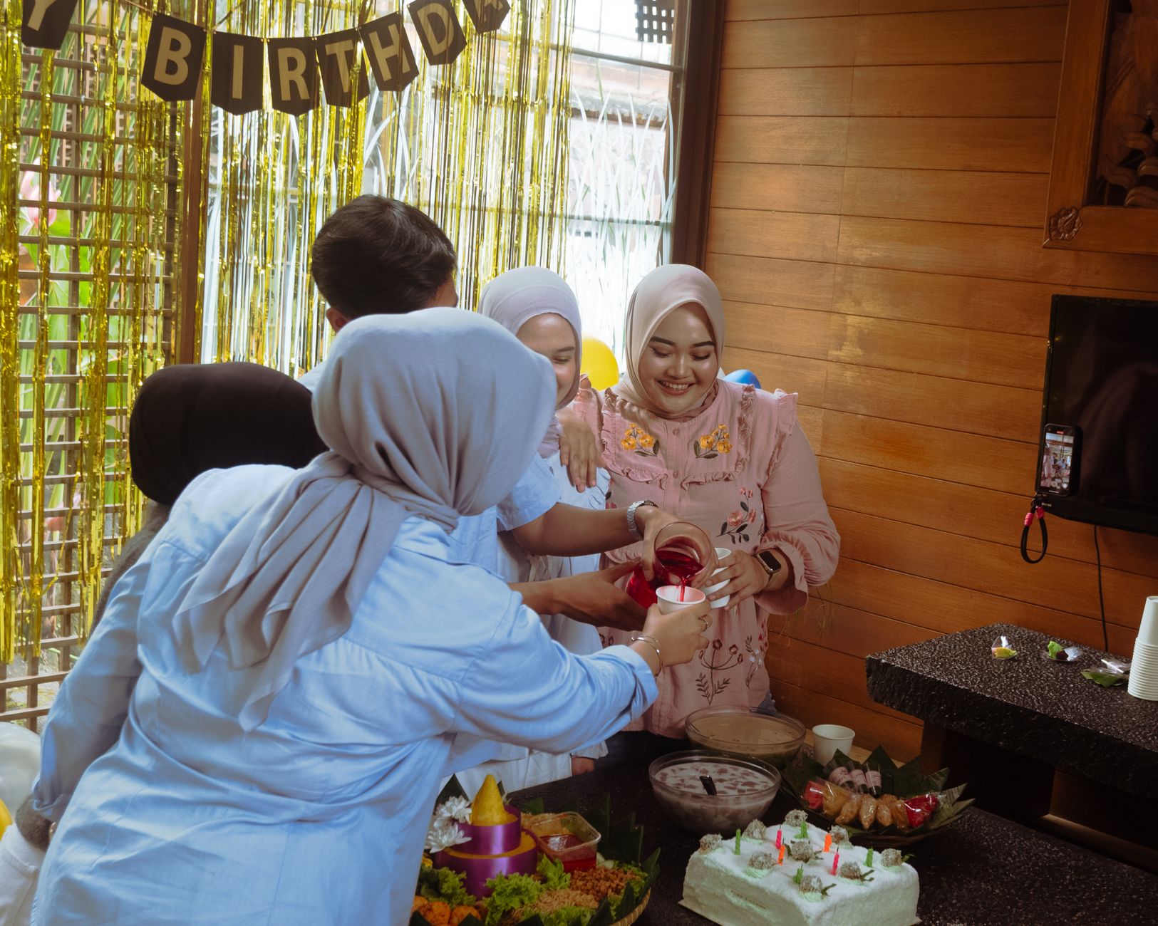 Group of adults celebrating a birthday indoors with food and decorations.