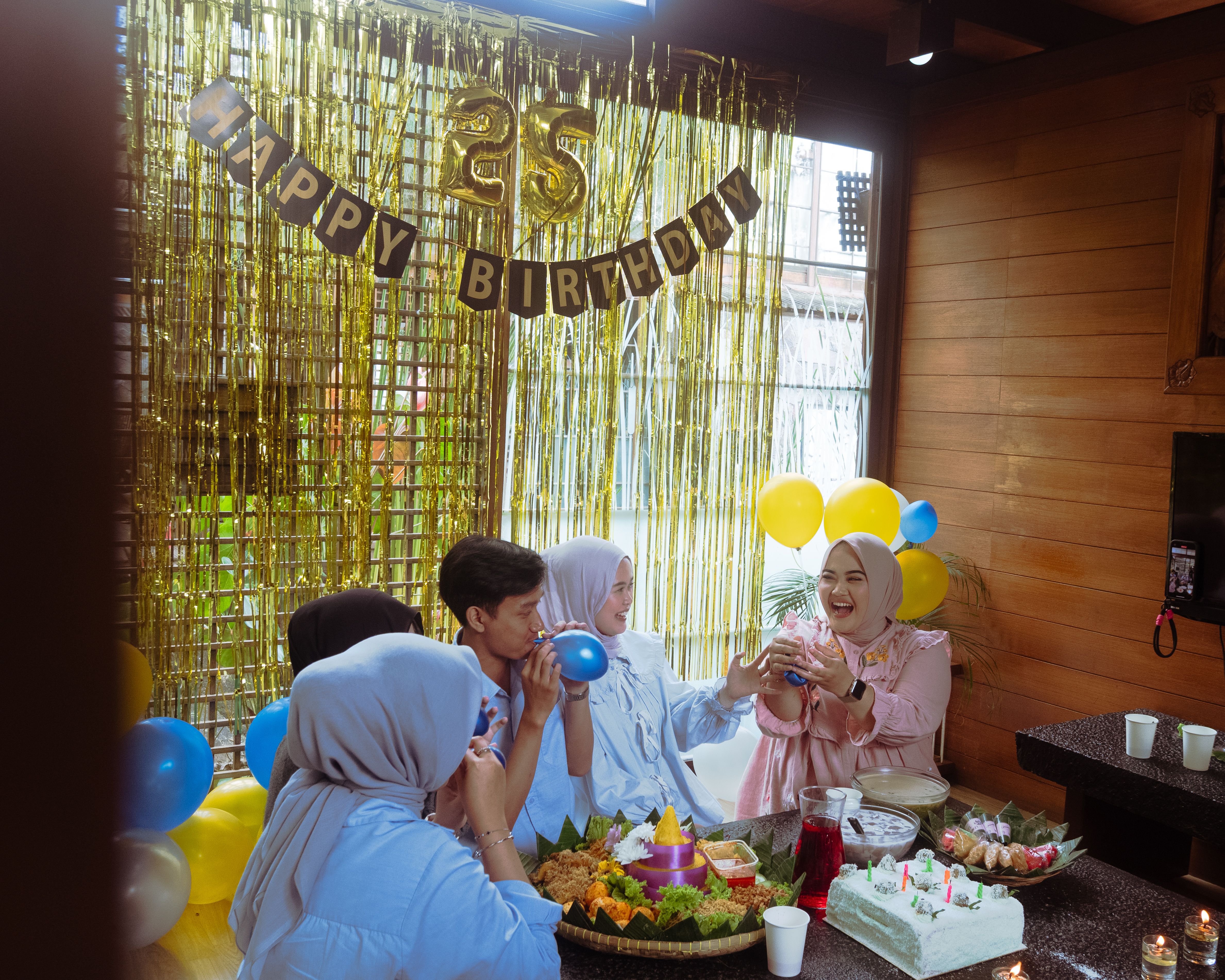 Group of friends celebrating a 25th birthday indoors with food and decorations.