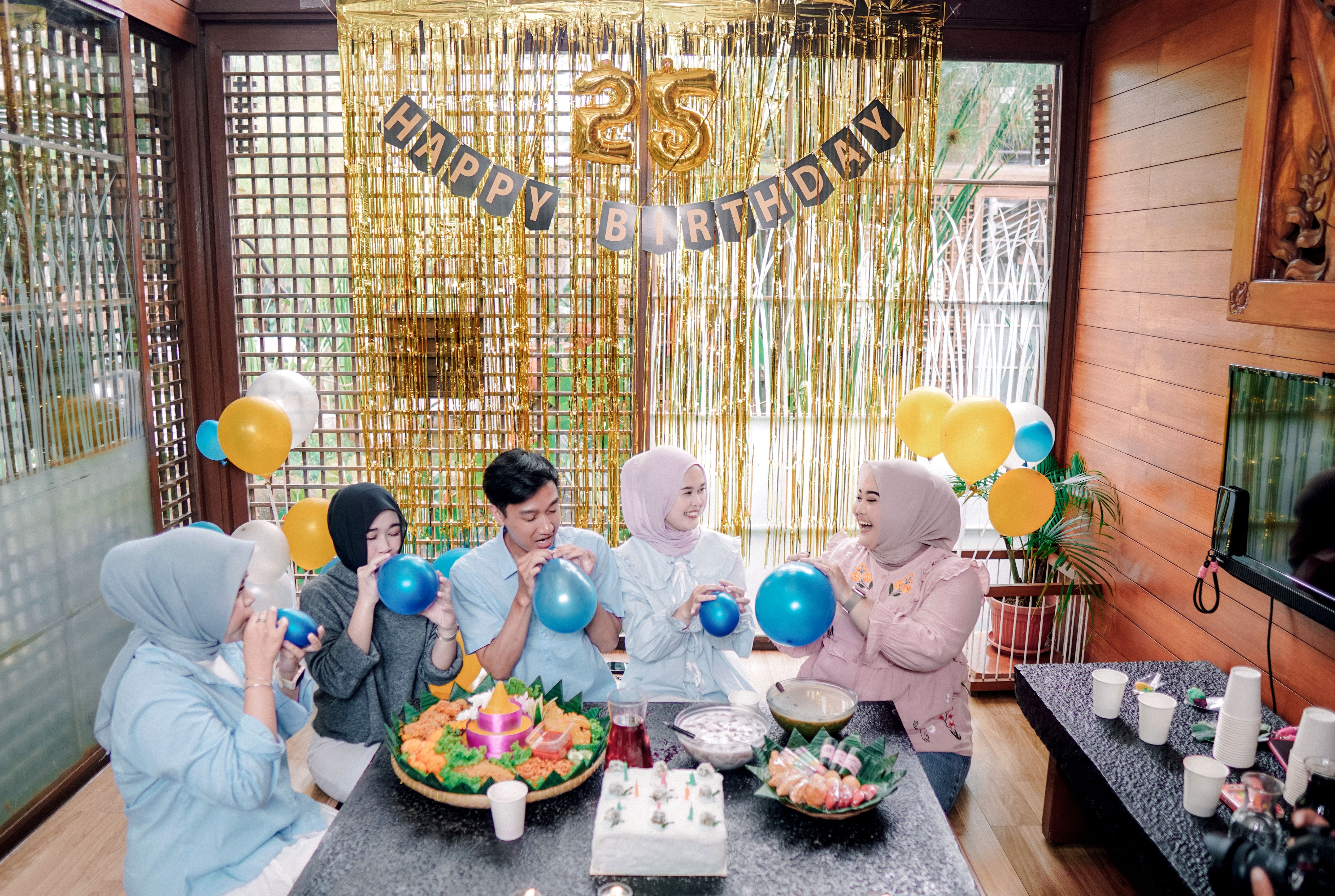 Group celebrating a 25th birthday indoors with balloons and food.