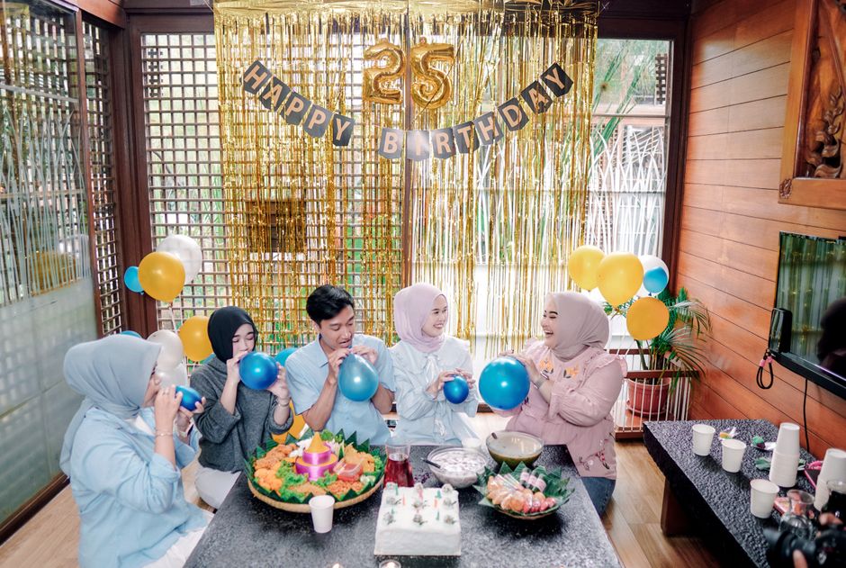 Group celebrating a 25th birthday indoors with balloons and food.