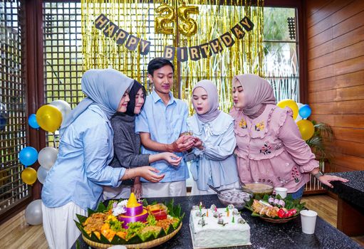 Group of five adults celebrating a 25th birthday party with food and decorations indoors.