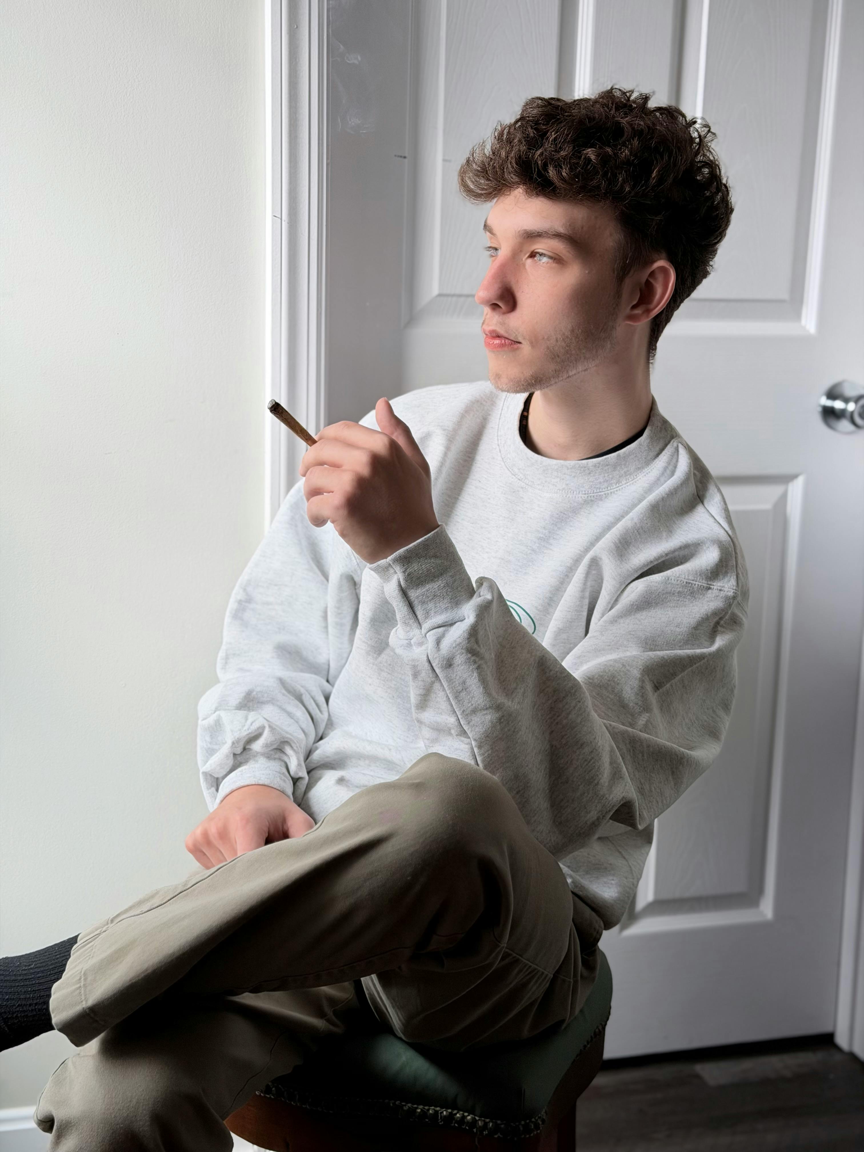 ingyenes Egy fiatalember elgondolkodva ül egy minimalista szobában a kezében cigarettával. Stockfotó