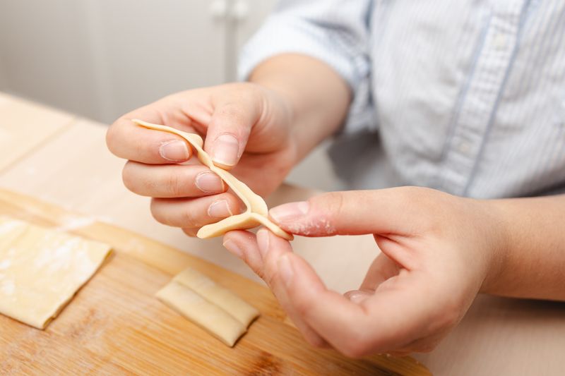 Hands skillfully shape fresh pasta dough on a wooden board in a cozy kitchen scene.