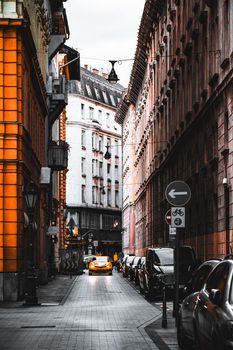 Dramatic view of a narrow Budapest street with vibrant architecture and a striking yellow car.