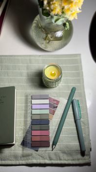 Elegant desk setup with pastel pens, candle, and flowers on a light green mat.