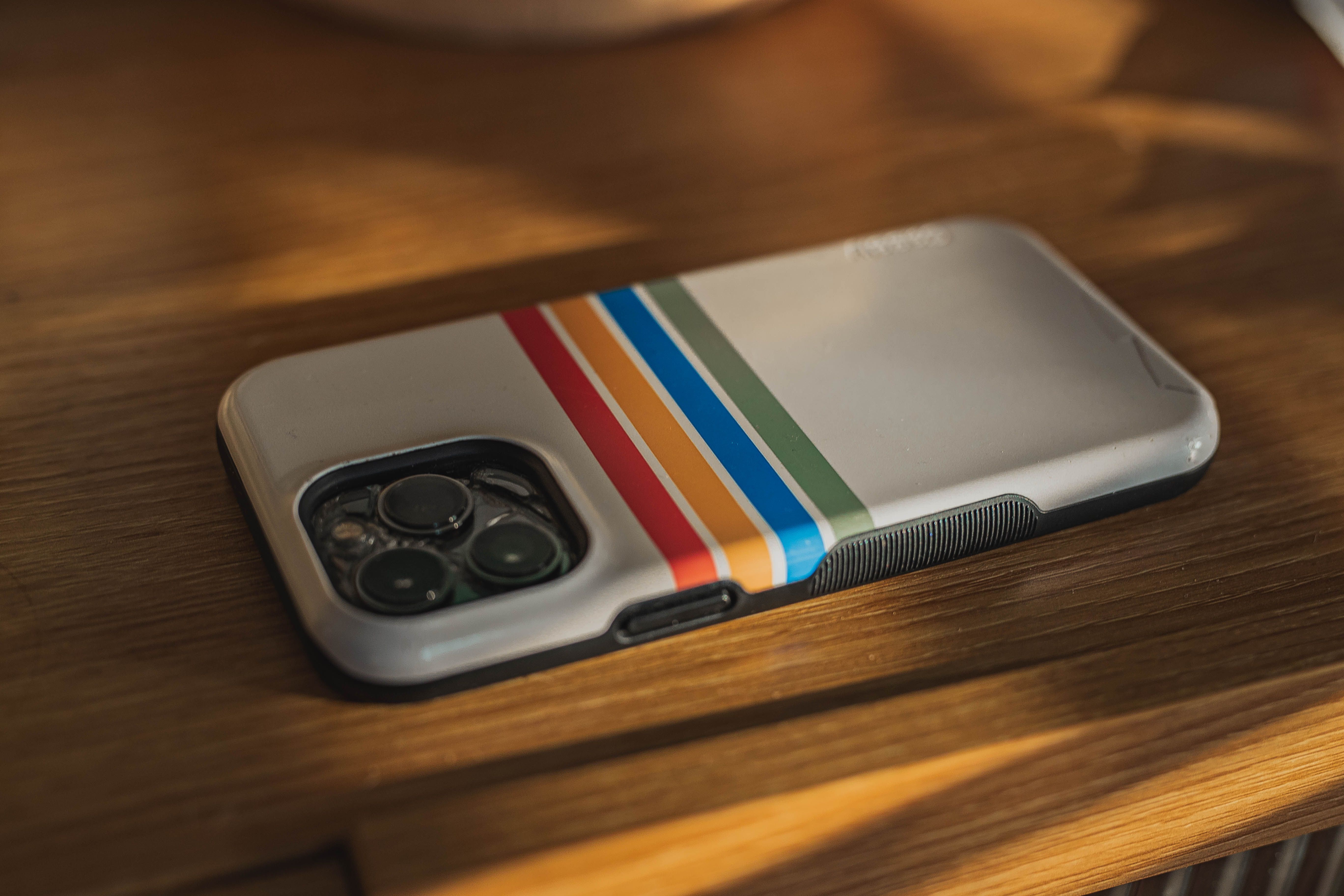 Close-up of an iPhone with a colorful retro case on a wooden surface, bathed in warm light.