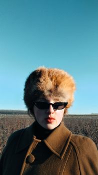 Stylish woman in vintage fashion outdoors wearing fur hat and sunglasses.