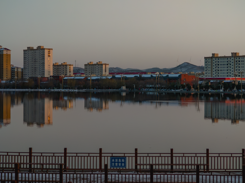 Free City buildings reflect on calm water during dusk with mountains in the background. Stock Photo